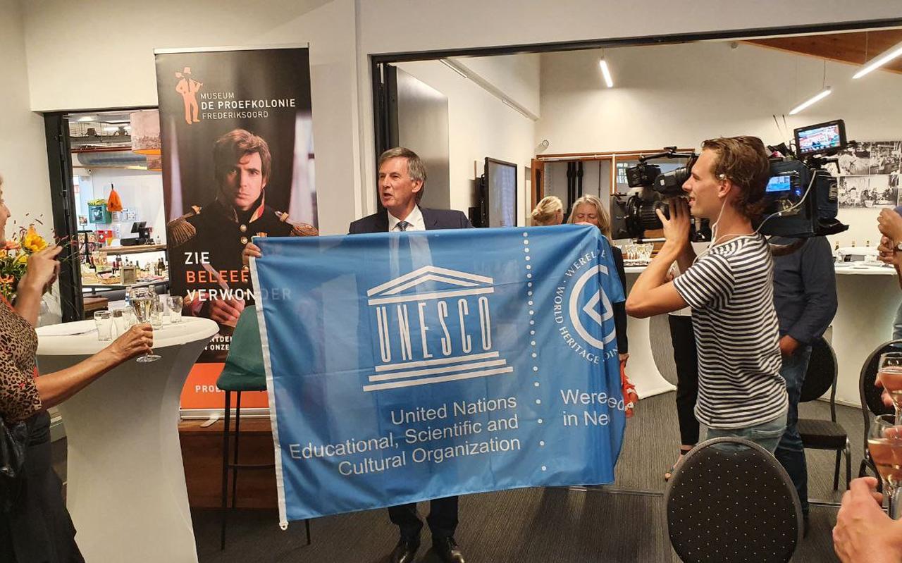 Gedeputeerde Cees Bijl laat na de toekenning van de werelderfgoedstatus trots de Unesco-vlag zien aan de zaal in Museum de Proefkolonie in Frederiksoord. Foto: DvhN Gedeputeerde Cees Bijl laat na de toekenning van de werelderfgoedstatus trots de Unesco-vlag zien aan de zaal in Museum de Proefkolonie in Frederiksoord. Foto: DvhN