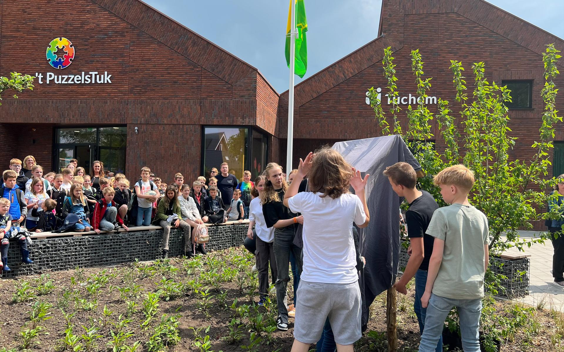 PuzzelsTuk-leerlingen die in schooljaar 2021 uitsroomden naar het voortgezet onderwijs onthullen hun afscheidcadeau: een insectenhotel, gemaakt door cliënten van de Maargieshoeve.
